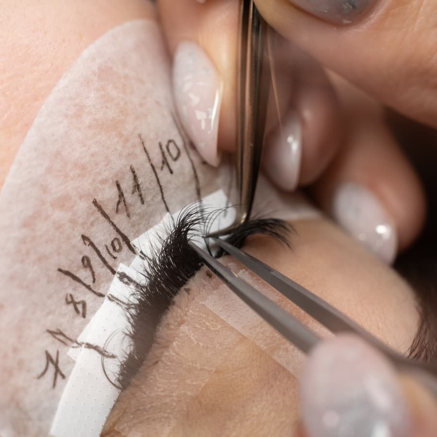 Lash artist applying eyelash extensions to a client in a modern studio
